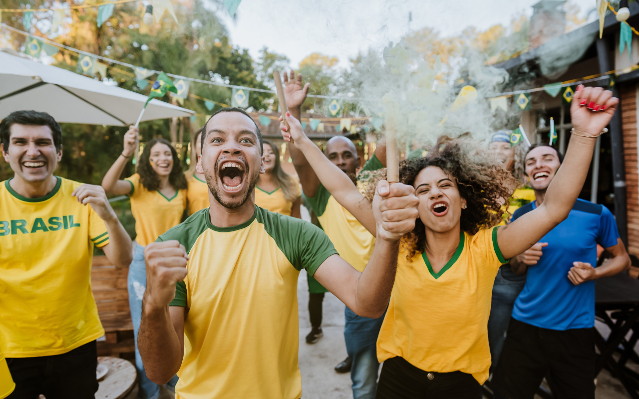 Torcedores brasileiros em um bar, com camisas verde e amarela, acompanhando um jogo pelo celular
